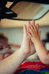 Oma ligt in rolstoel en geeft high five aan haar kleinzoon. Een volwassen hand en een peuterhand raken elkaar. Intiem moment dankzij zorg en pgb van Per Saldo.
