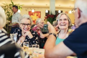 Gasten van de Buurtmaaltijd van Solidez Welzijn in Wageningen lachen en praten samen met buurtgenoten tijdens een gezellig en ongedwongen moment.