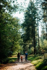 Esther, Tim en dochter Marin wandelen hand in hand over een bospad, met blonde peuter Marin in het midden. Vastgelegd in een natuurlijke en authentieke fotografie stijl.