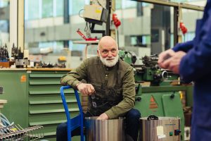 Otto, een oudere instrumentmaker met een opvallende witte baard, werkt in een technische werkplaats van de Universiteit Utrecht tussen machines en hergebruikte onderdelen, als voorbeeld van zero waste en circulair werken.