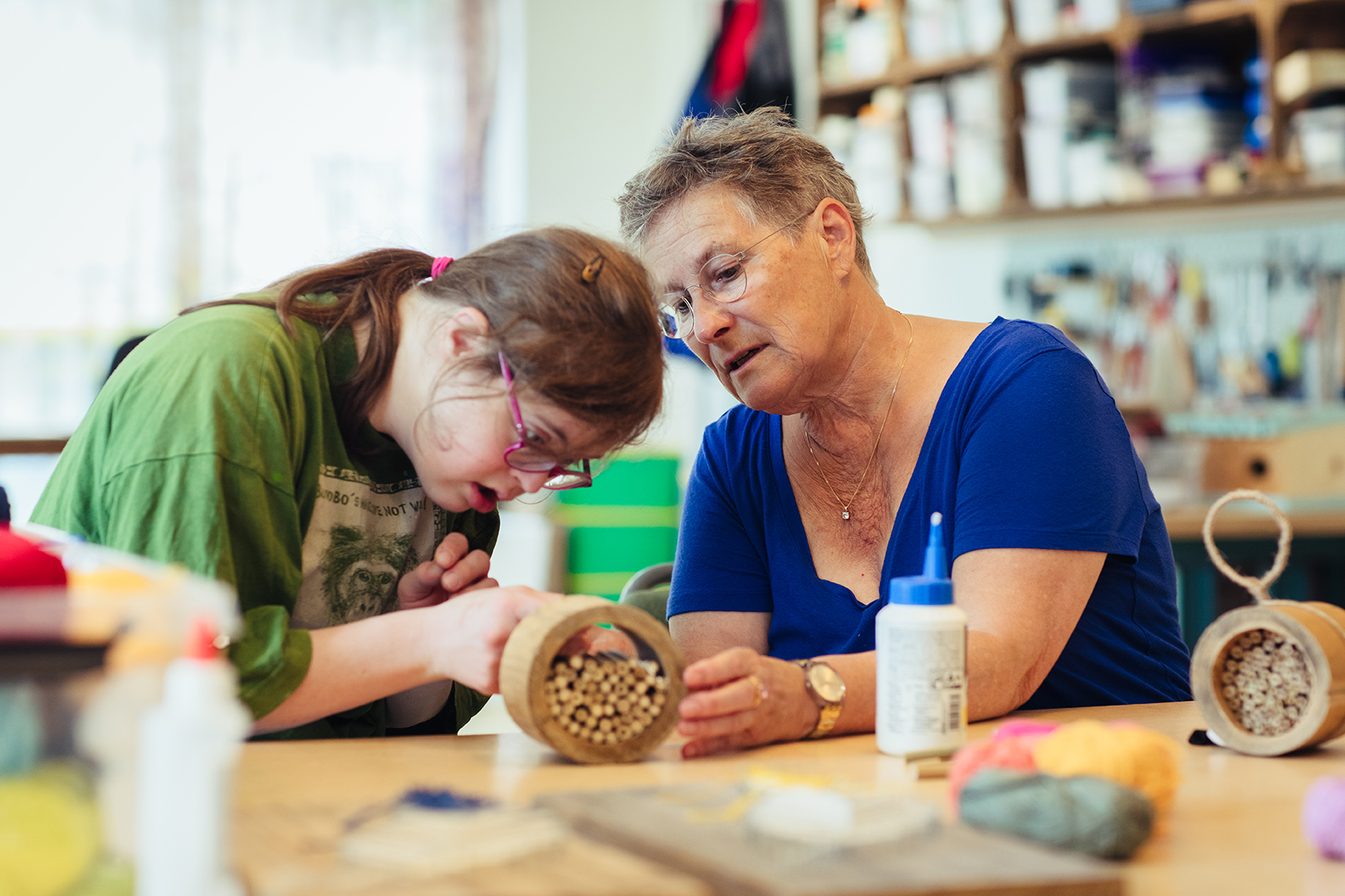 Een vrijwilliger van Eigenhandig, onderdeel van Zideris, ondersteunt een jonge vrouw met een verstandelijke beperking tijdens de dagbesteding. Ze werken samen aan een creatief project, terwijl de vrijwilliger met zachte aandacht naast haar zit. Het moment straalt geduld, verbondenheid en echte betrokkenheid uit.
