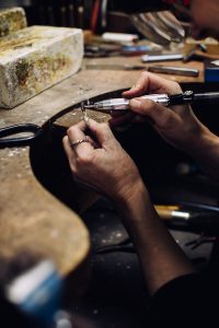 Close-up van de handen van Vivianne Veenemans die met aandacht en een fijn slijpgereedschap een sieraad bewerkt aan haar werkbank in haar atelier.