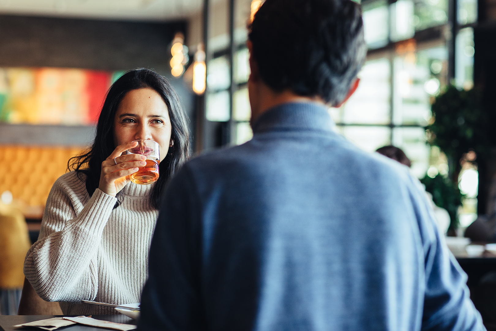 Een vrouw neemt glimlachend een slok van haar drankje tijdens een diner bij De Blaauwe Kamer in Wageningen, terwijl gesprekken, zacht daglicht en de warme sfeer van het wereldse buffetrestaurant zorgen voor een ontspannen moment samen.
