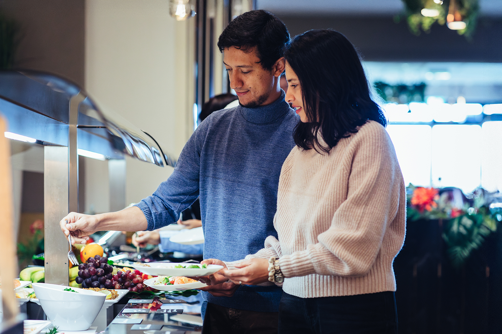 Een man en een vrouw scheppen samen eten op bij het wereldse buffet van De Blaauwe Kamer in Wageningen, waar kleurrijke wereldgerechten, ontmoeting en samen genieten centraal staan.