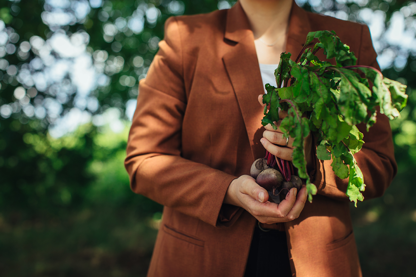 Voedingsdeskundige Stefi Fens houdt een bosje vers geoogste rode bieten met loof in haar handen, tegen een zachte, groene achtergrond. Een sfeervol moment van oogst, pure voeding en de verbinding tussen gezondheid en lokale, seizoensgebonden producten.