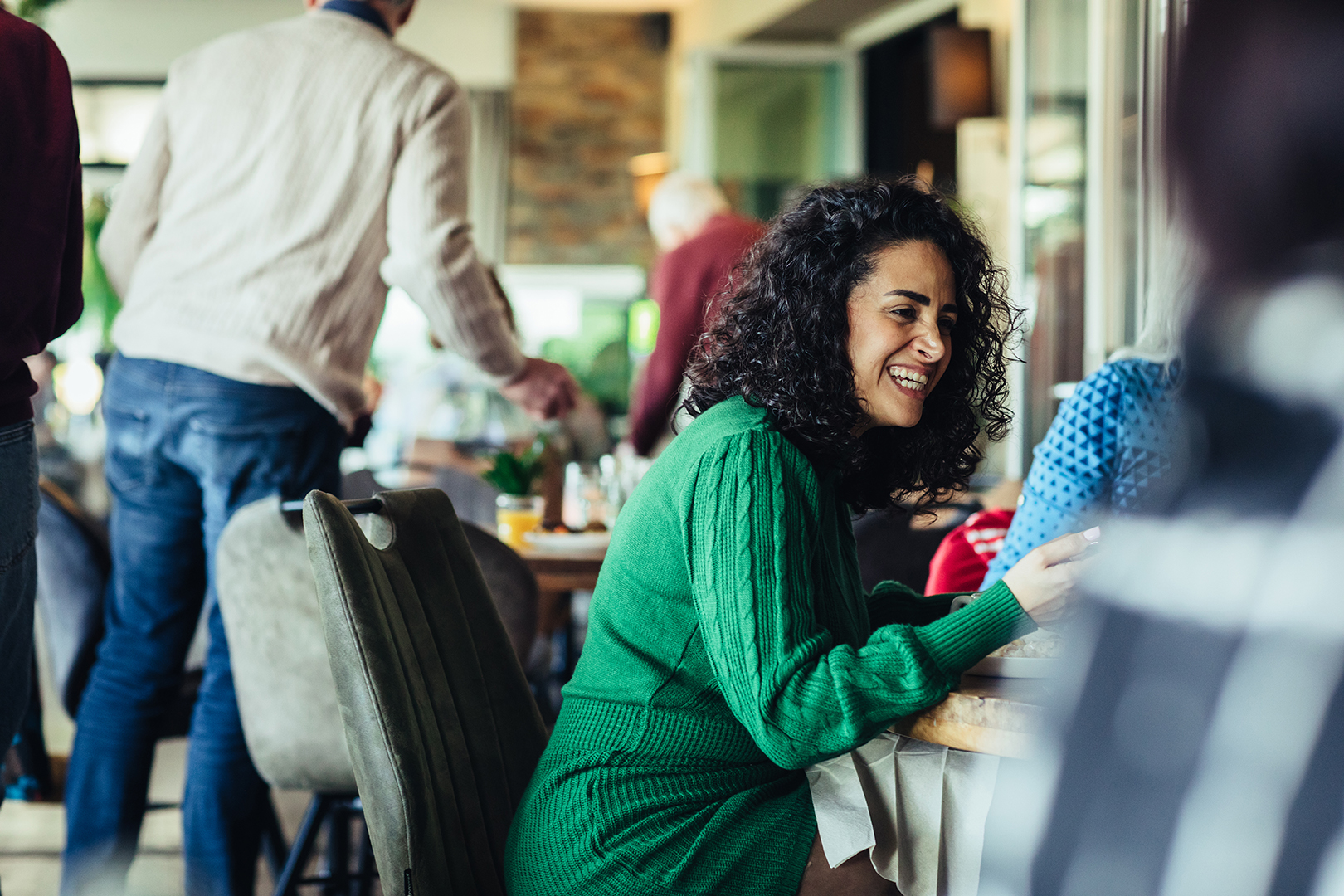 Gasten genieten samen van een diner bij De Blaauwe Kamer in Wageningen, terwijl een vrouw in een groene jurk lachend aan tafel zit tussen gesprekken, wereldse gerechten en de warme sfeer van een wereldkeuken buffetrestaurant.