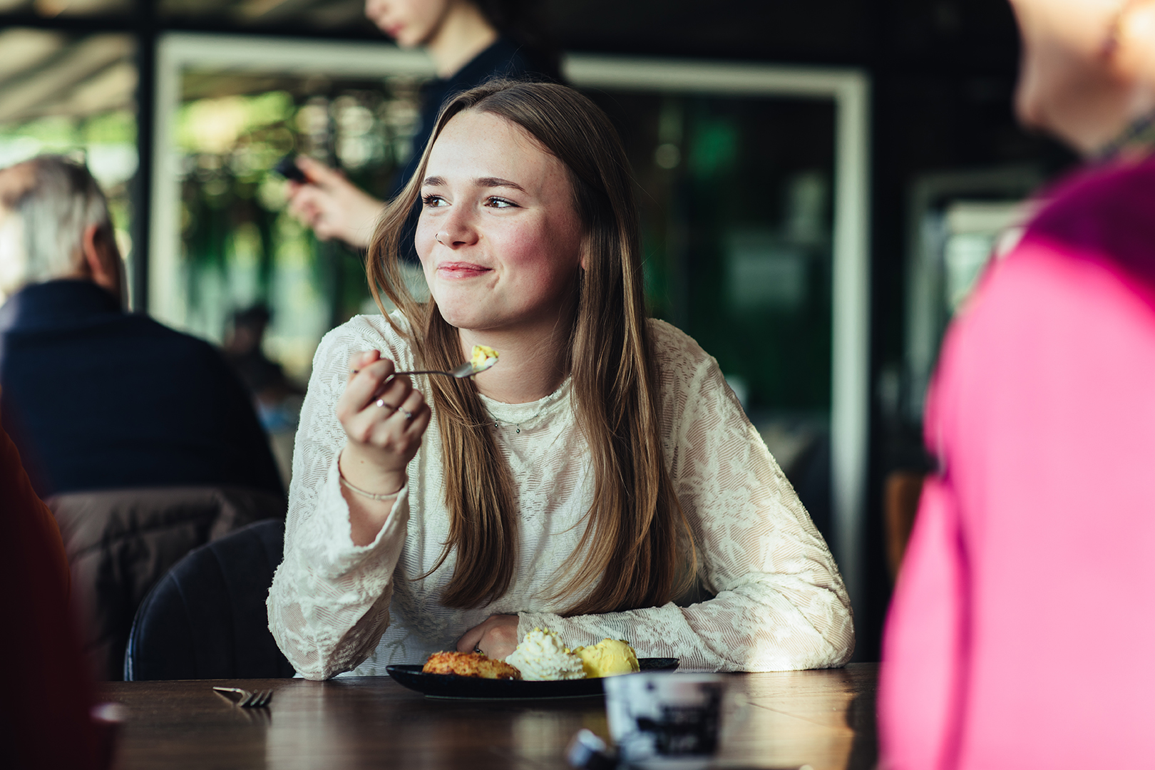 Een jonge vrouw proeft glimlachend een dessert aan tafel bij De Blaauwe Kamer in Wageningen, terwijl gesprekken, zachte middagzon en de ontspannen sfeer van een wereldkeuken buffetrestaurant zorgen voor een warm en spontaan moment van samen genieten.