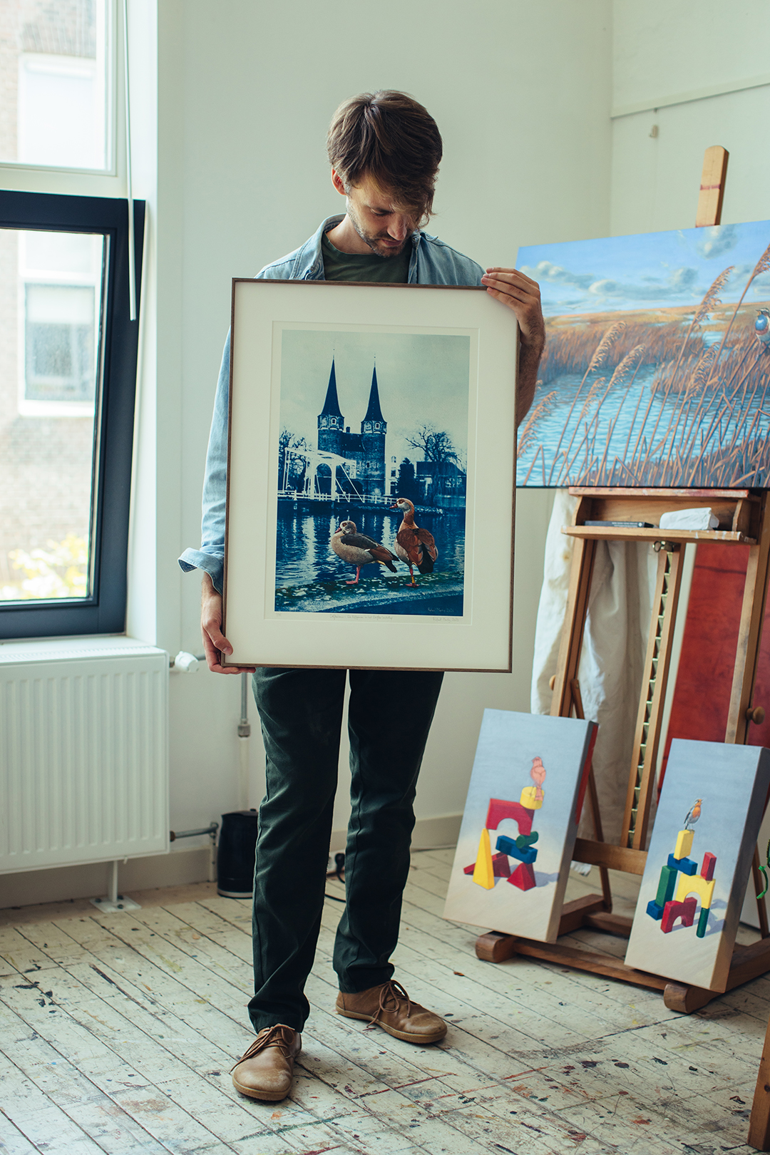 Rafael staat bij het raam van zijn lichte atelier en houdt een ingelijst schilderij voor zich. Op het werk is een stedelijk landschap van Delft in blauwdruk te zien, met op de voorgrond ganzen in kleur geschilderd. Achter hem staan andere schilderijen en doeken tegen de muur.
